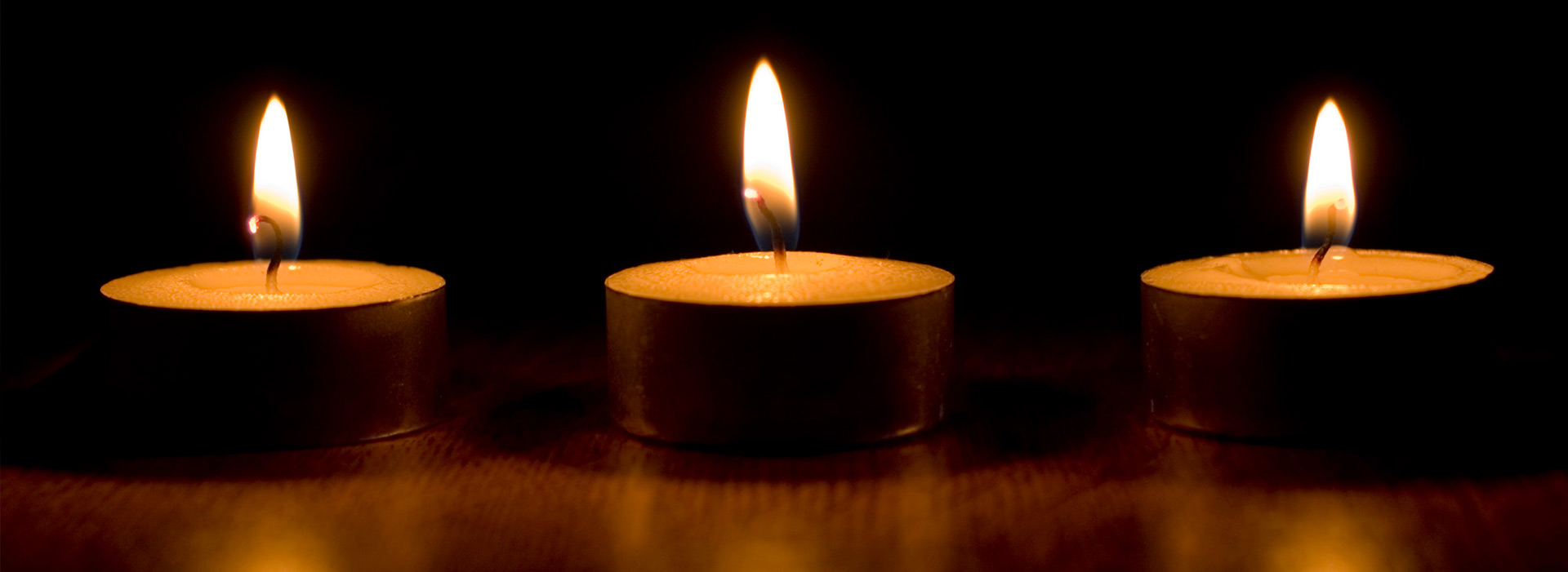 Drei brennende Kerzen auf dunklem Hintergrund.